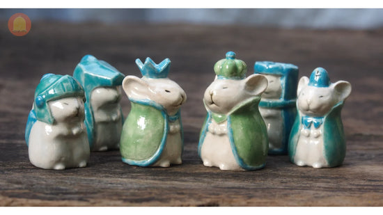 Cute ceramic mouse figurines in blue and green crowns and capes on wooden surface
