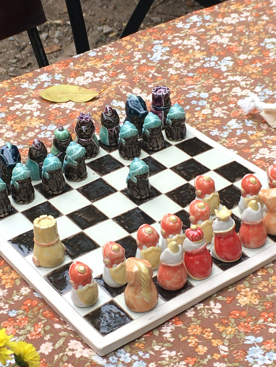 Handcrafted clay chess set with colorful figurines on floral tablecloth